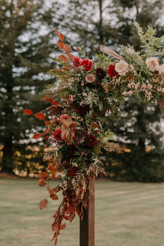wedding arch dotted with brown red wedding floral and greenery for fall wedding colors 2023 emerald and brown